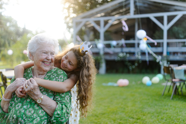Young girl hugging her elderly grandmother at a garden party. Love and closeness between grandparent and grandchild.