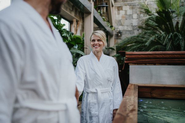 Beautiful couple in spa robes standing in hotel greenhouse, looking at each another, enjoying romantic wellness weekend in the spa. Concept of Valentine's Day.
