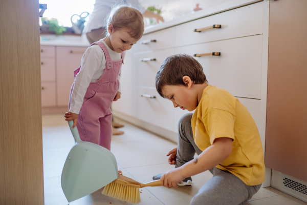 A little boy and girl helping to clean house using pan and brush as they sweep up dirt off floor.