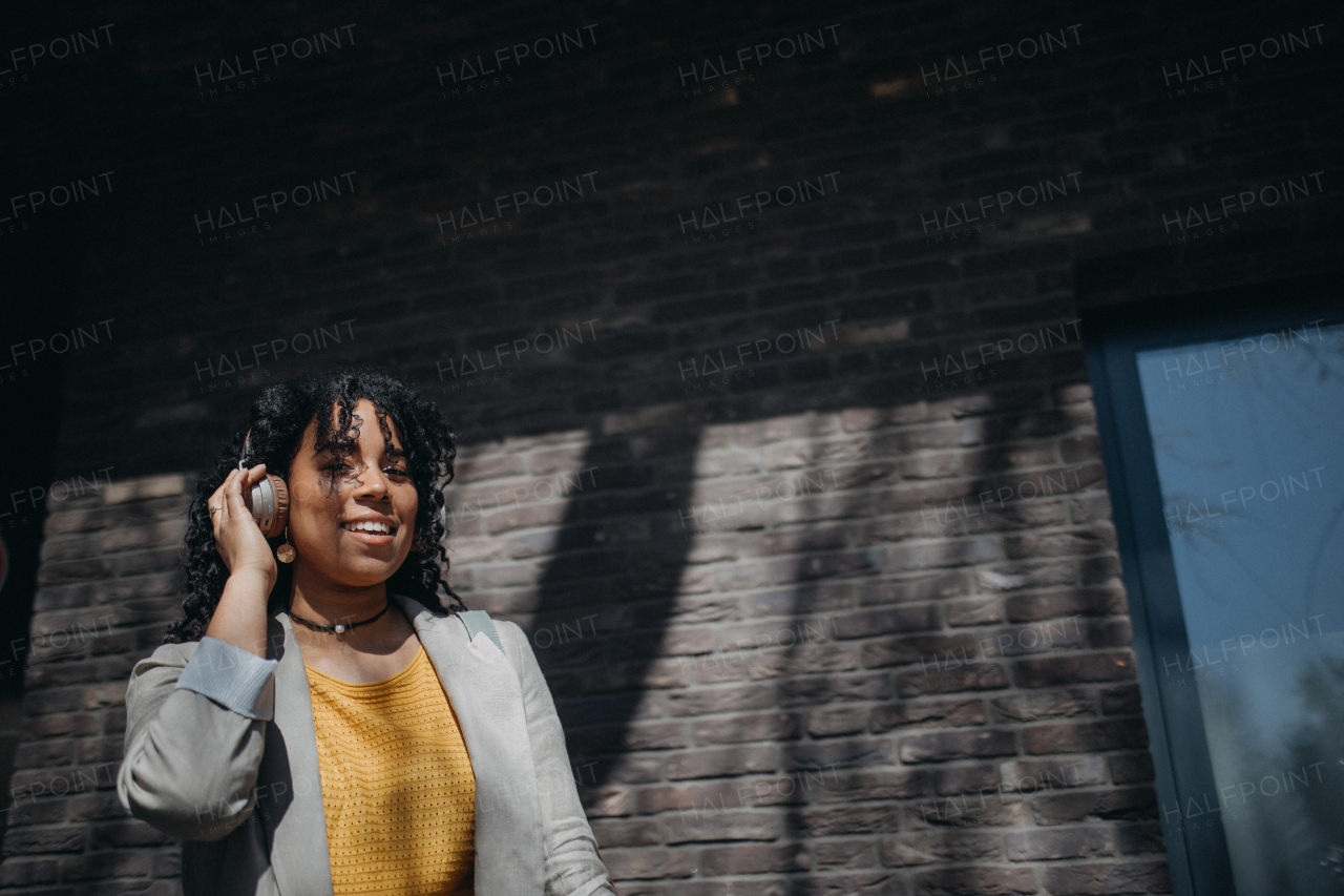 A young biracial woman wearing headphones and enjoying listening to music outdoors in street.