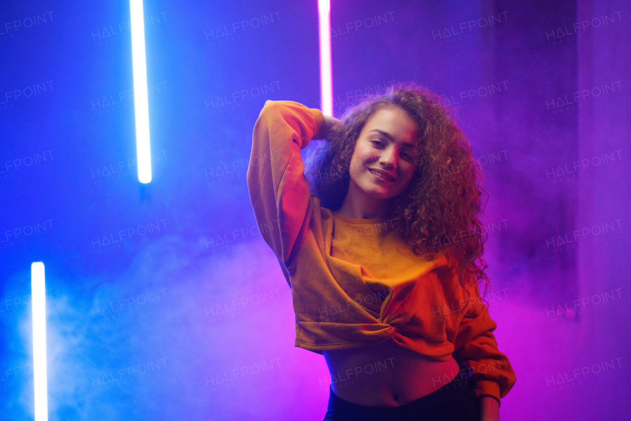 A portrait of a happy young woman dancing over neon light background at disco party