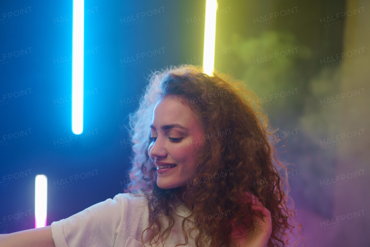 A portrait of a happy young woman dancing over neon light background at disco party