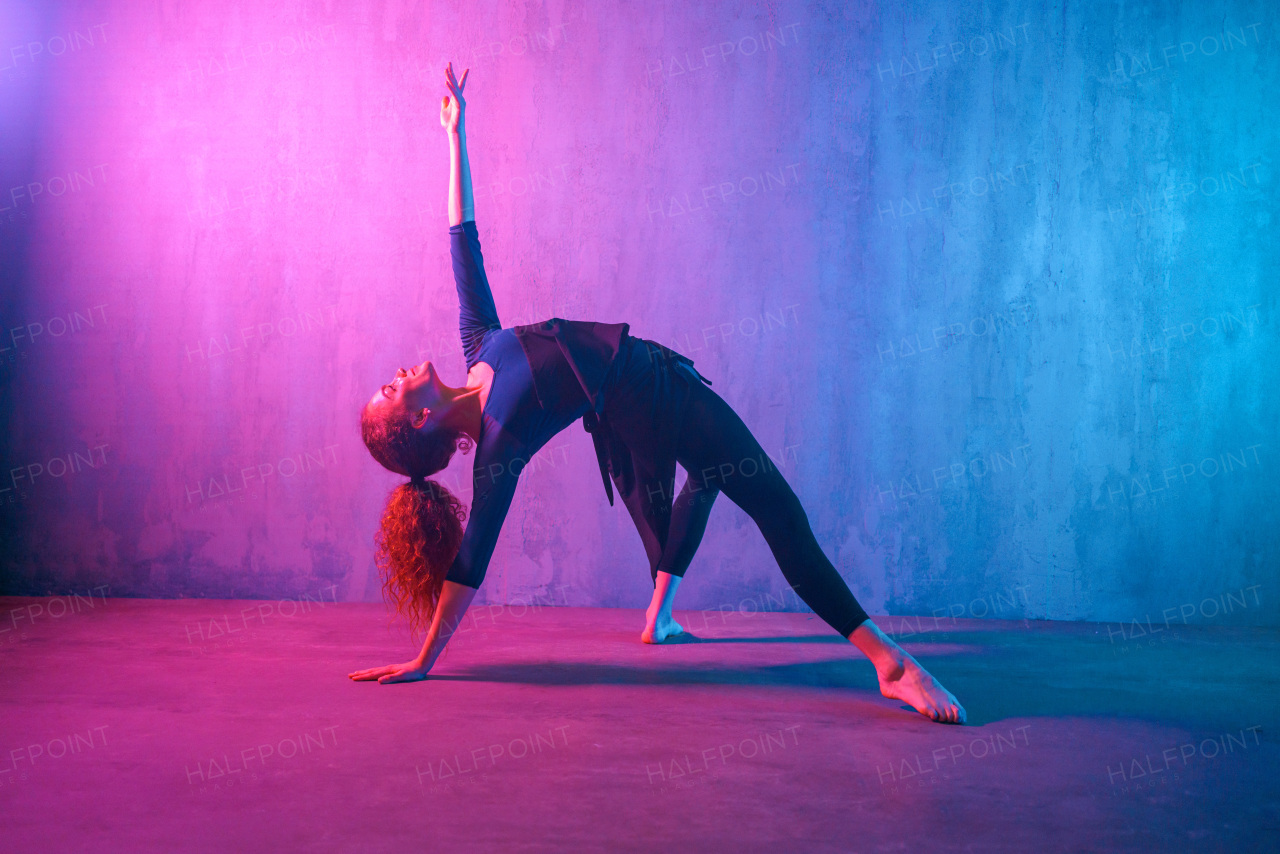 A modern dance girl dancer dancing in neon light doing gymnastic exercises in studio, copy space.