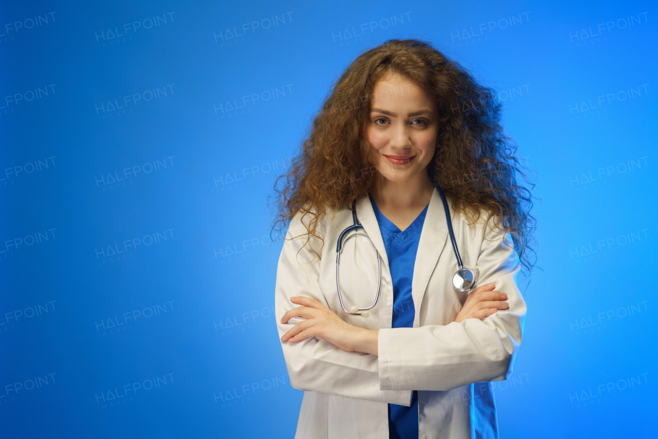 A studio shot of a young female doctor looking at camera against a blue background.
