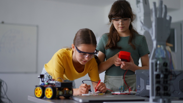 Two girl classmates working togeter on circuit board, building robotic car in an after-school robotics club. Children learning robotics in Elementary school.