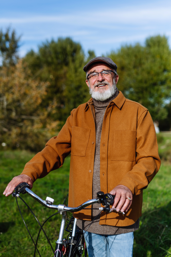 Portrait of friendly older man with gray beard. Senior standing outdoors in nature, looking at camera and smiling.