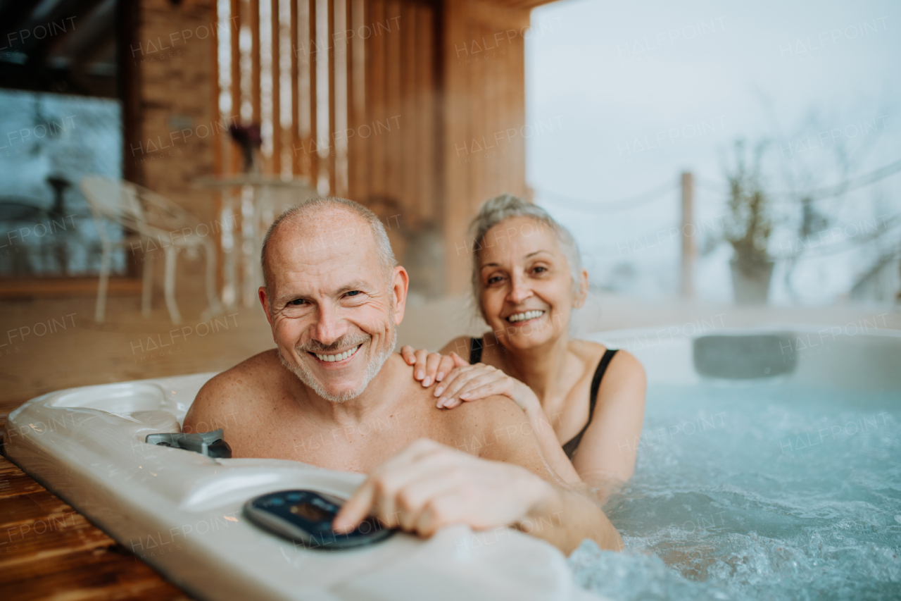 Senior couple enjoying together outdoor bathtub at their terrace during a cold winter day.