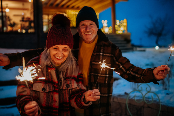 Happy senior couple celebrating new year with the sparklers, enjoying winter evening.