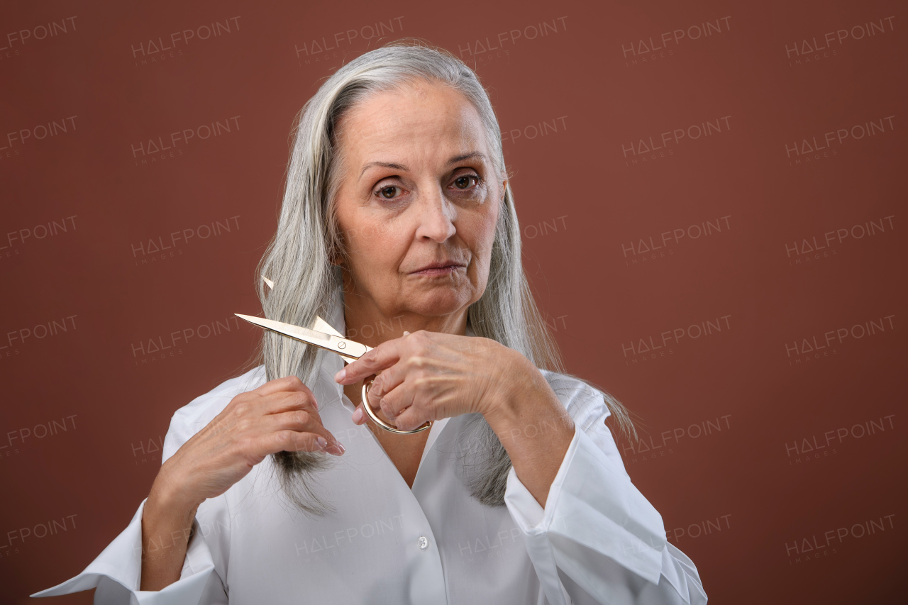 Portrait of unhappy senior woman cutting her hair because of breast cancer. Breast cancer awareness concept.