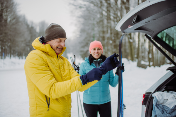 Senior couple near a car trunk preparing for winter hiking, putting on gloves.