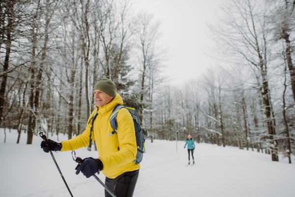 Senior man doing cross country skiing in front of a snowy forest.