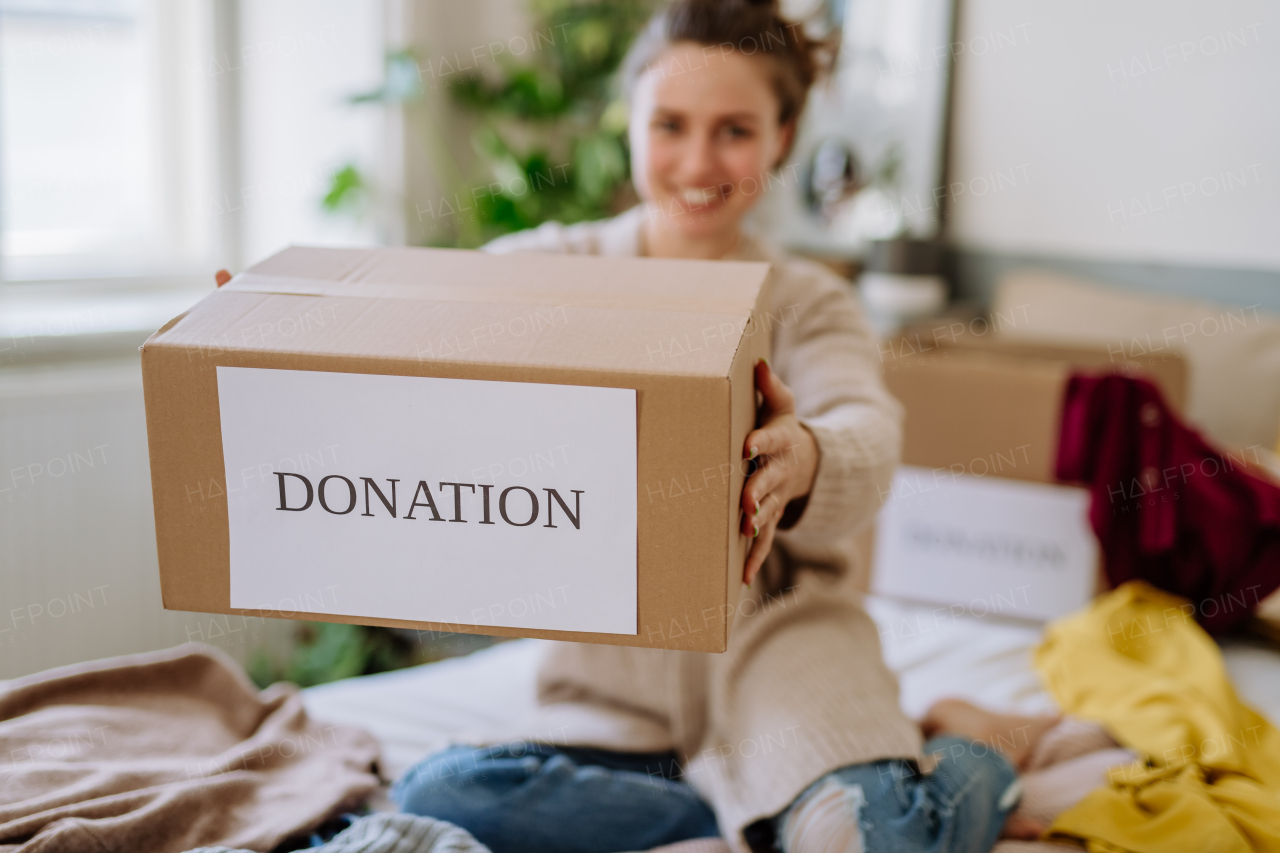 Young woman giving her clothes packed in box to charity.
