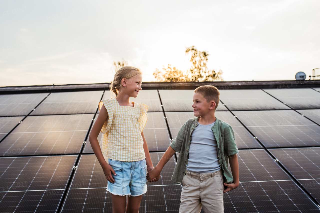 Two young siblings on roof with solar panels, looking at each other.Sustainable future for next generation concept.