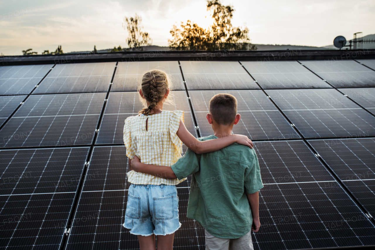 Two young siblings on roof with solar panels, holding each other.Sustainable future for next generation concept.
