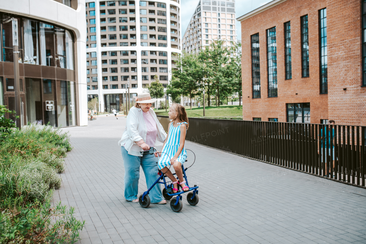 Grandma with walker and granddaugter in the city, on walk. Girl spending time with senior grandmother, during holidays, after school.
