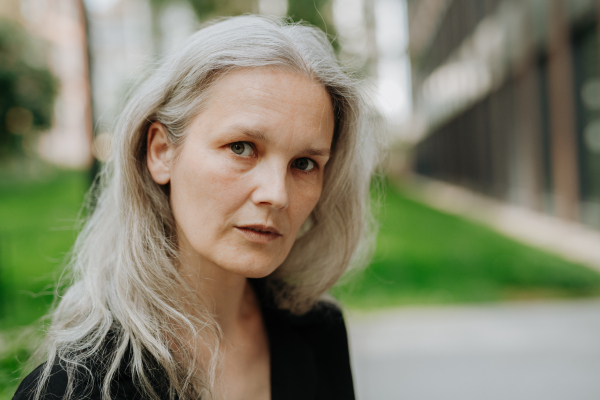 Portrait of beautiful mature woman in middle age with long gray hair, standing outdoor in the city.