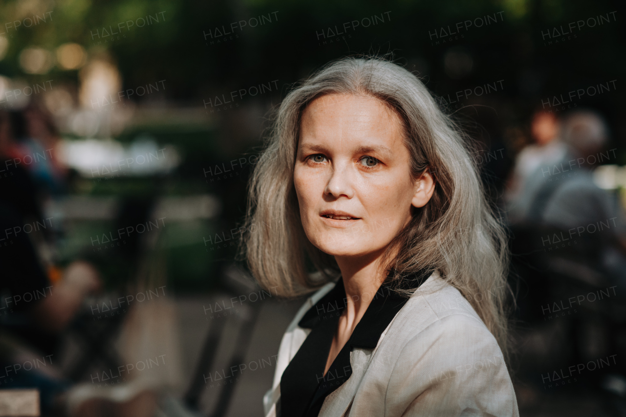Portrait of beautiful mature woman in middle age with long gray hair, smiling and standing outdoor in the city.