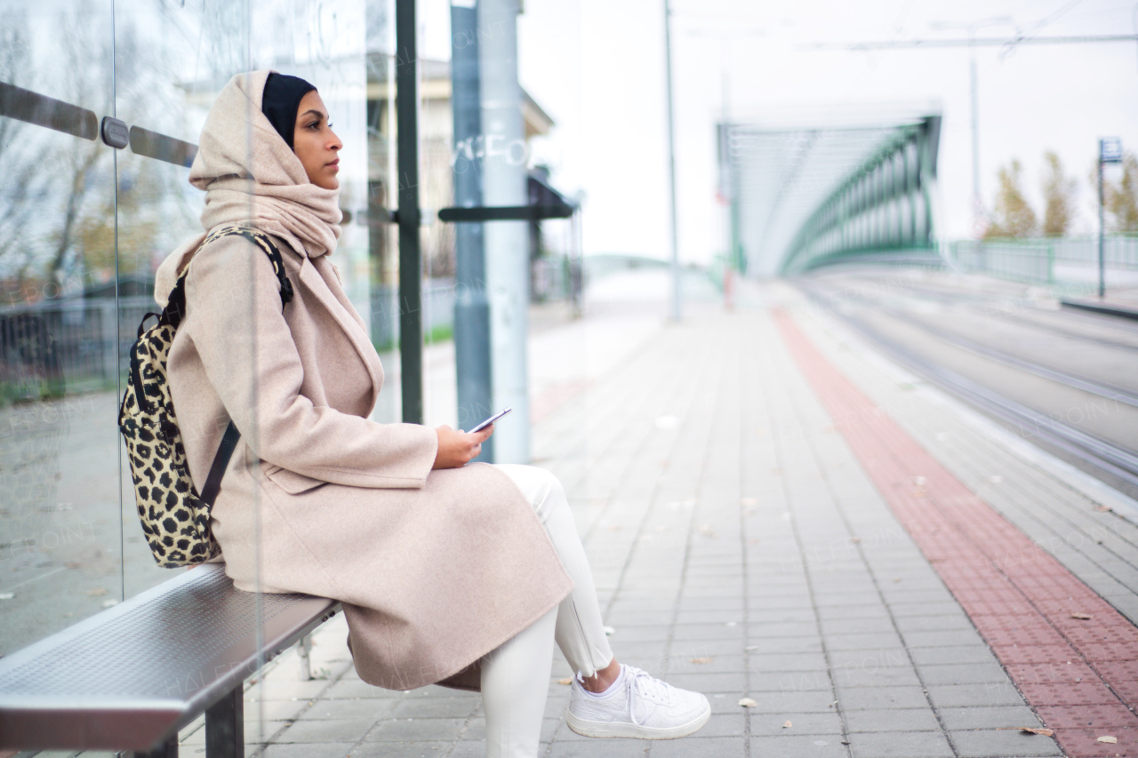 Young muslim woman waiting for a bus at city bus stop.