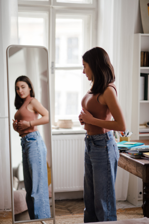 Young teenage girl looking in the mirror in the room.