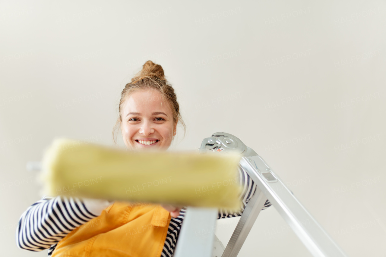 Happy young woman remaking her new house, painting walls. Concept of renovation, indepent women and sustainable lifestyle.