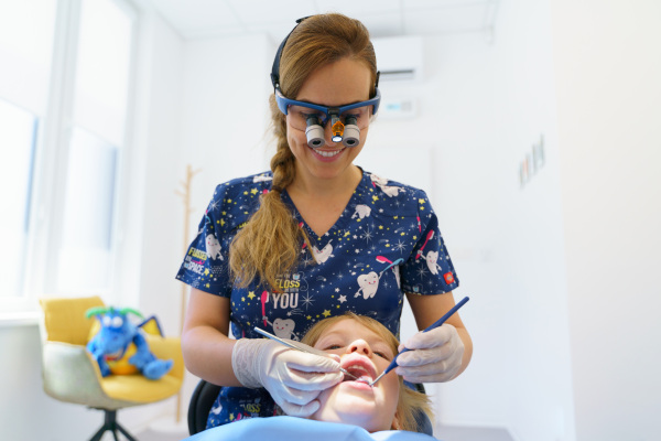 Young woman dentist doing doing preventive examination a little girl.