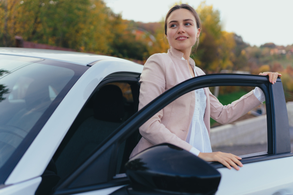 Excited young woman getting out of a car.