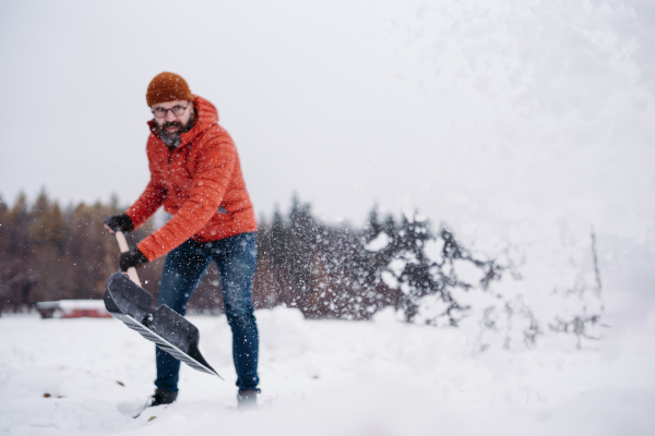 Man shoveling snow with shovel, cleaning driveway in front of his house. Scooping and throwing snow, shoveling.