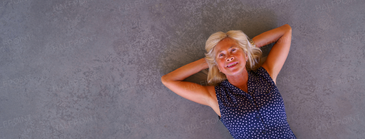 Happy senior woman lying at a concrete floor, wide photography. Copy space.