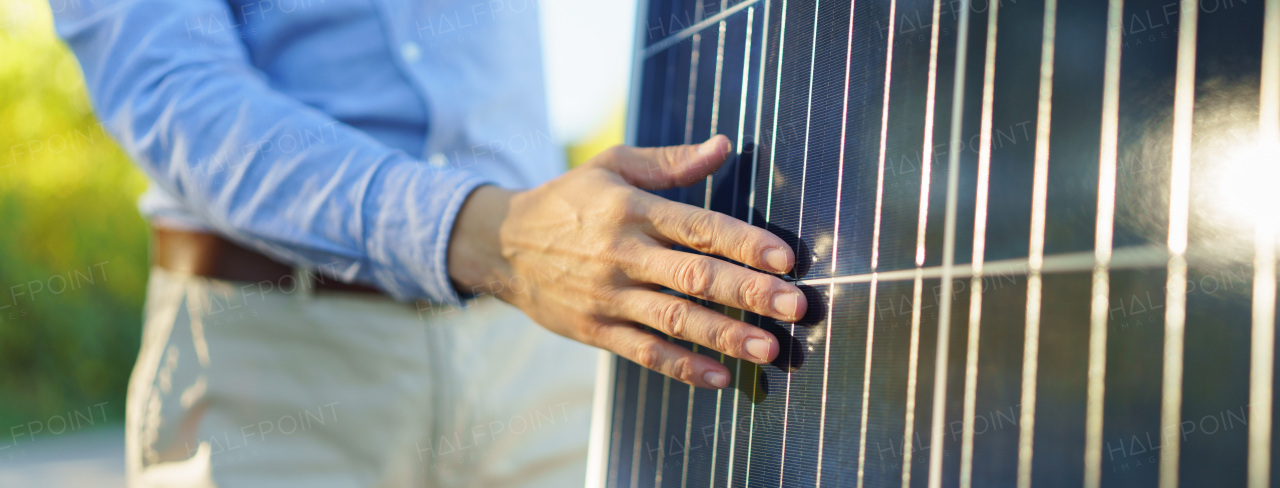 Close-up of businessman holding solar panel, standing outdoor at a garden.