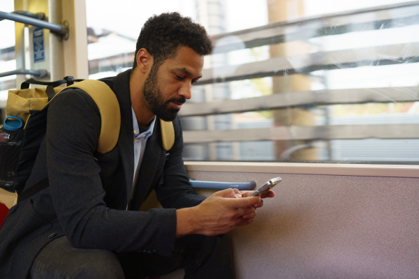 Handsome man traveling by city train, scrolling on a smartphone. Man heading home after a long work day. Single man using dating app.