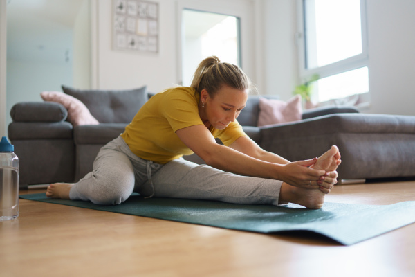 Woman exercising at home, stretching body. Single woman is happy, relaxed, and content with her life. Solo home workout and meditation, morning or evening workout routine.