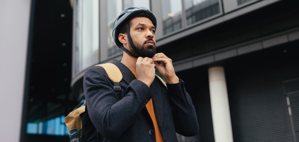 City commuter, businessman traveling from work to home on a bike, fastening helmet for safety. City lifestyle of single man. Banner with copyspace.