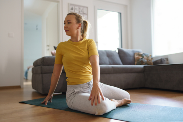 Woman exercising at home, stretching body. Single woman is happy, relaxed, and content with her life. Solo home workout and meditation, morning or evening workout routine.