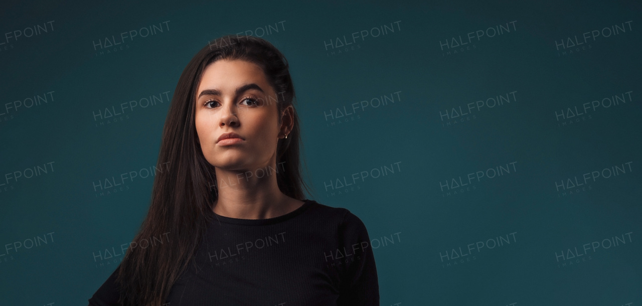 Portrait of a young woman in studio, dark blue background.
