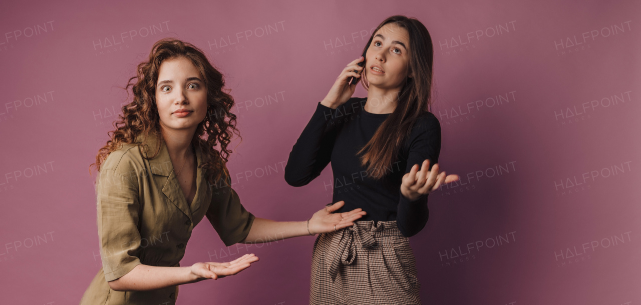 Studio shoot of two young women, one has long call with a mobile phone.