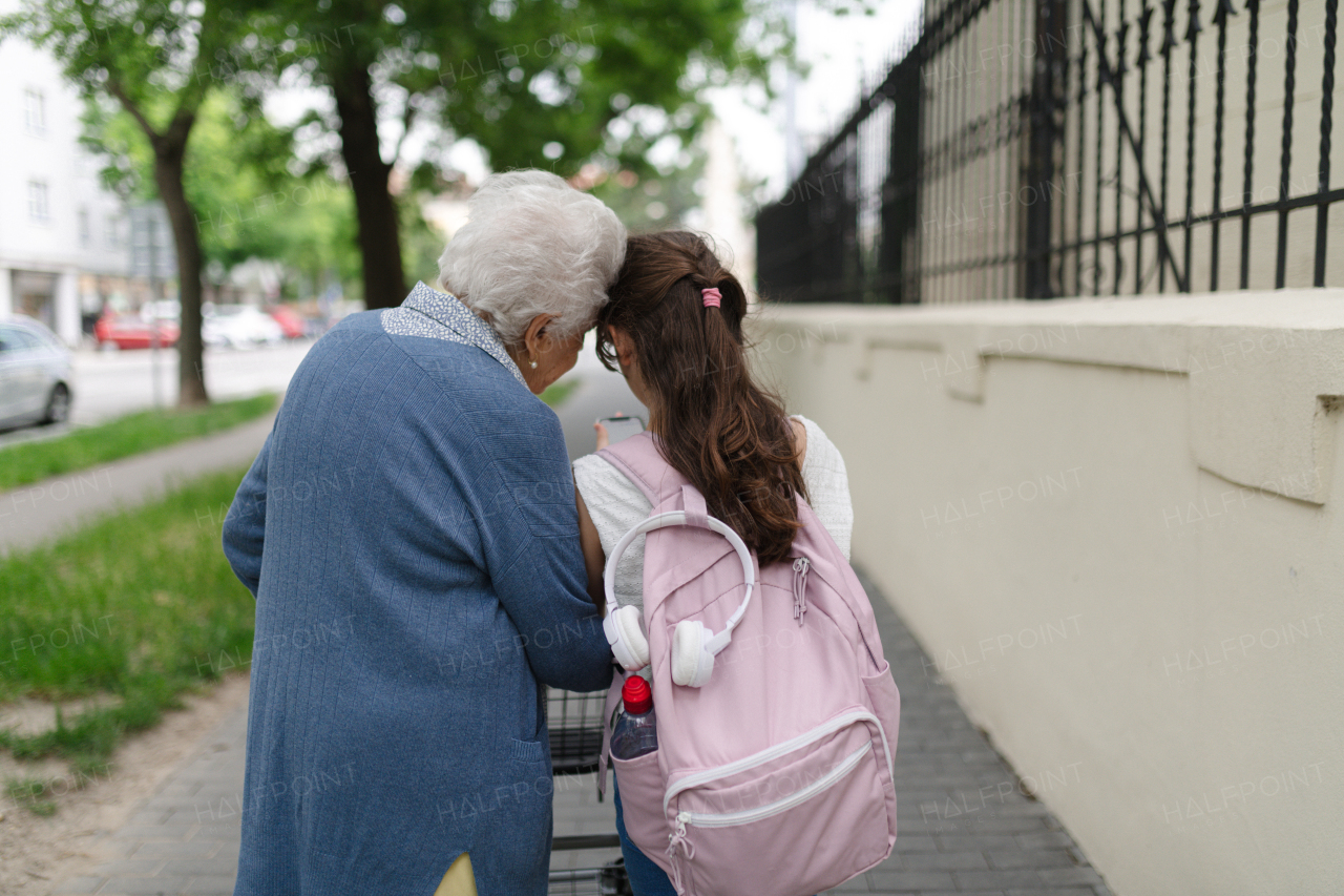Grandma picking up girl after first day of school. Granddaughter spending time with her senior grandmother outdoors in the city, walking.