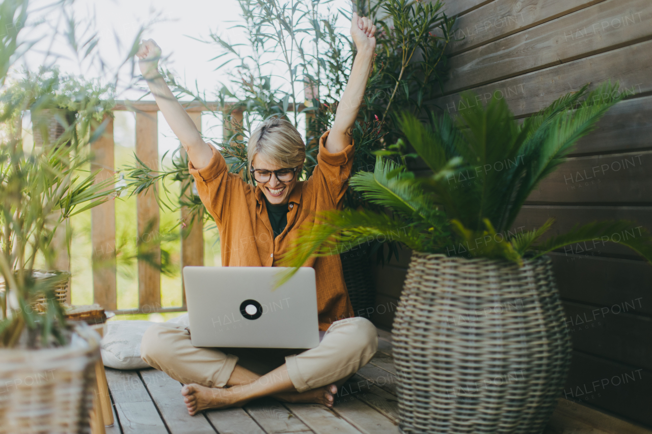 Woman working in garden, , with laptop on legs, celebrating success Businesswoman working remotely from outdoor homeoffice. Concept of outdoor home office.