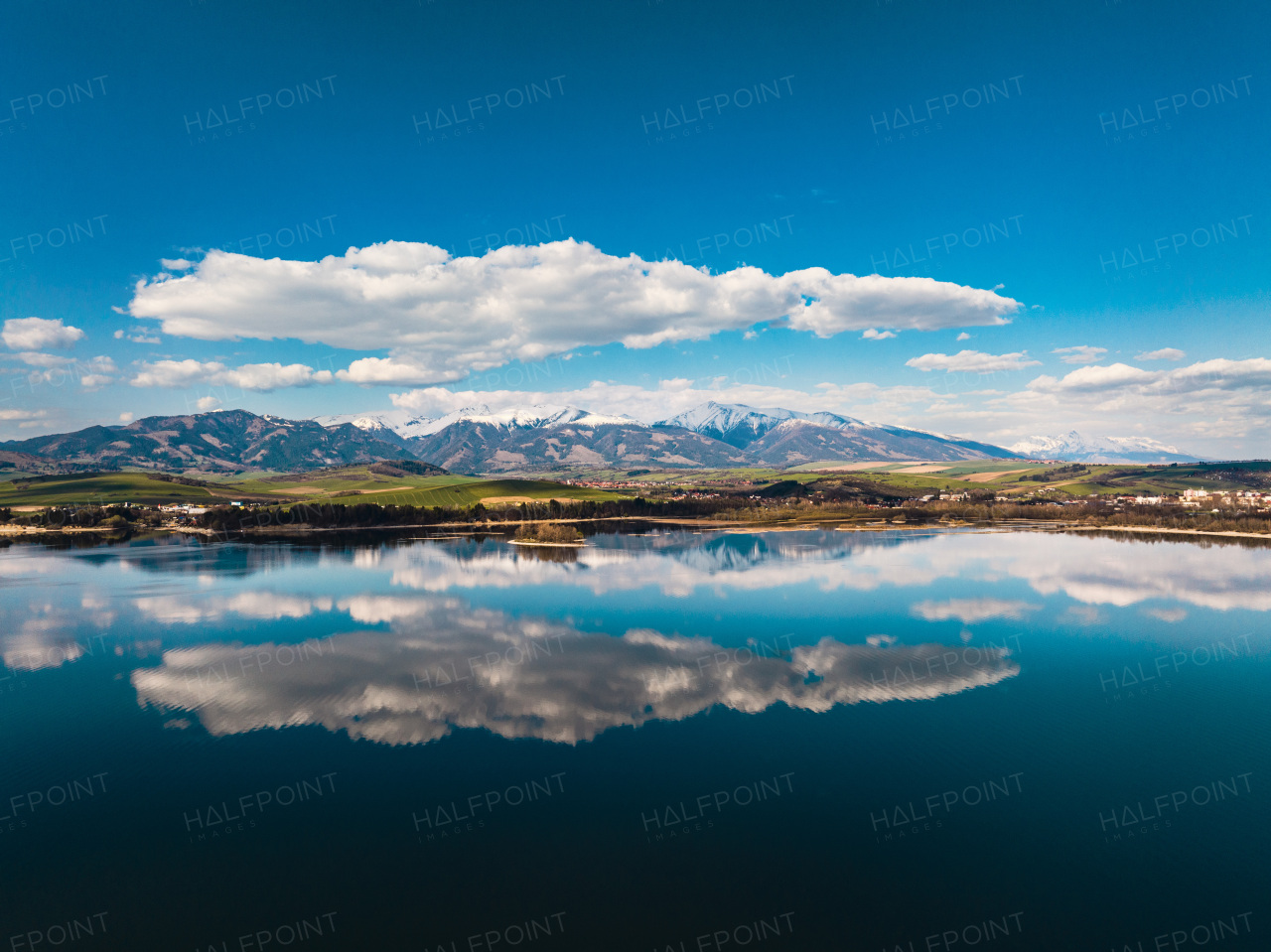 Aerial view from above the water surface of Liptovska Mara water reservoir on serene nature landscape, High Tatras Mountains in the distance.
