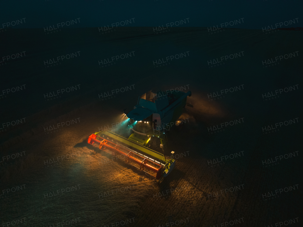 Aerial view of a tractor a harvester working on field during night. Agriculture and cultivation of industrial farms. Agribusiness.