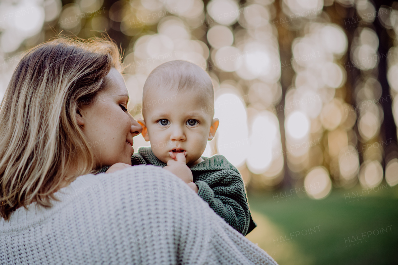 A mother holding her little baby son wearing knitted sweater during walk in nature, close-up