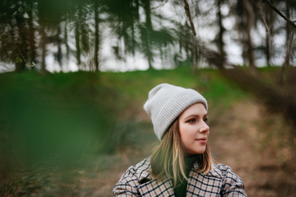 Portrait of young woman in coat and knitted cap in autumn nature, walking in a forest.