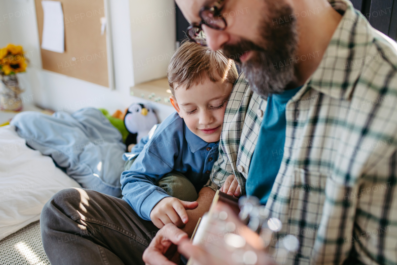 Father teaching boy to play on acoustic guitar. Mesmerized son listening dad making music. Concept of Fathers Day, and fatherly love.