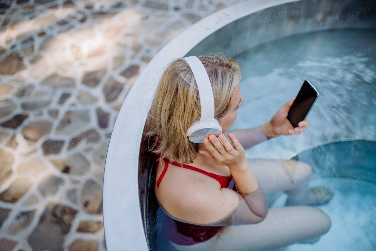 A rlaxed woman wearing headphones listening to music and sittin in hot tub, summer vacation concept.