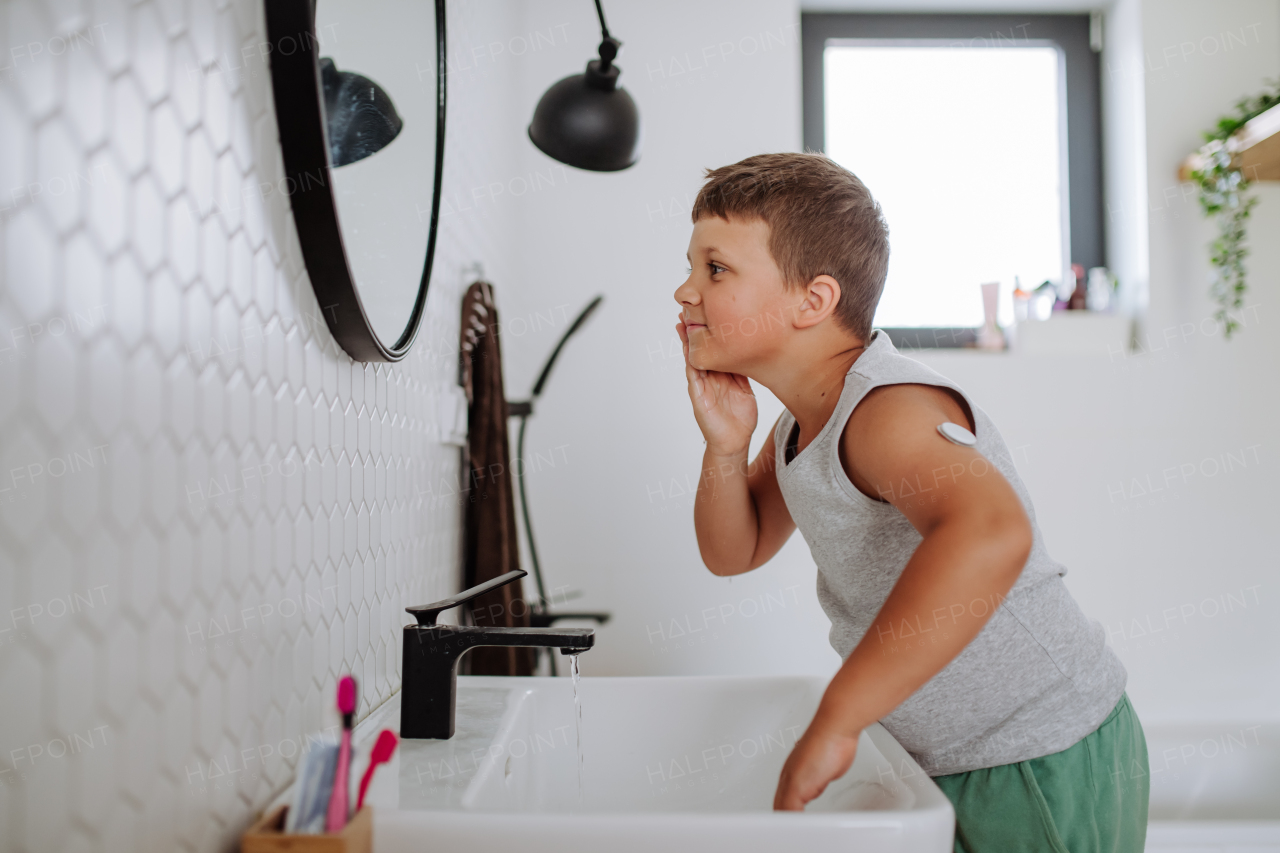 The diabetic boy getting ready in the morning, while wearing a continuous glucose monitoring sensor on his arm. CGM device making life of school boy easier, helping manage his illness and focus on other activities.
