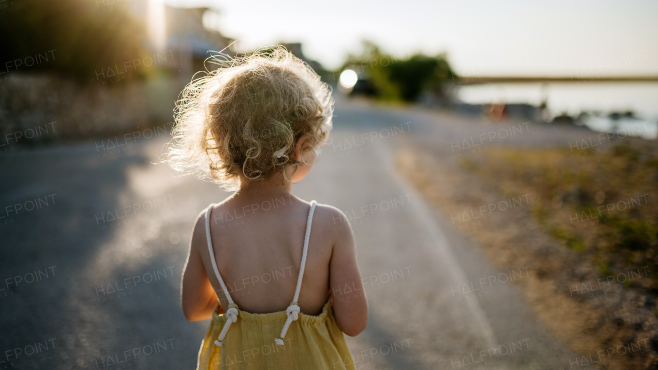 Rear view of blonde girl in summer outfit on walk during summer vacation, beach holiday.