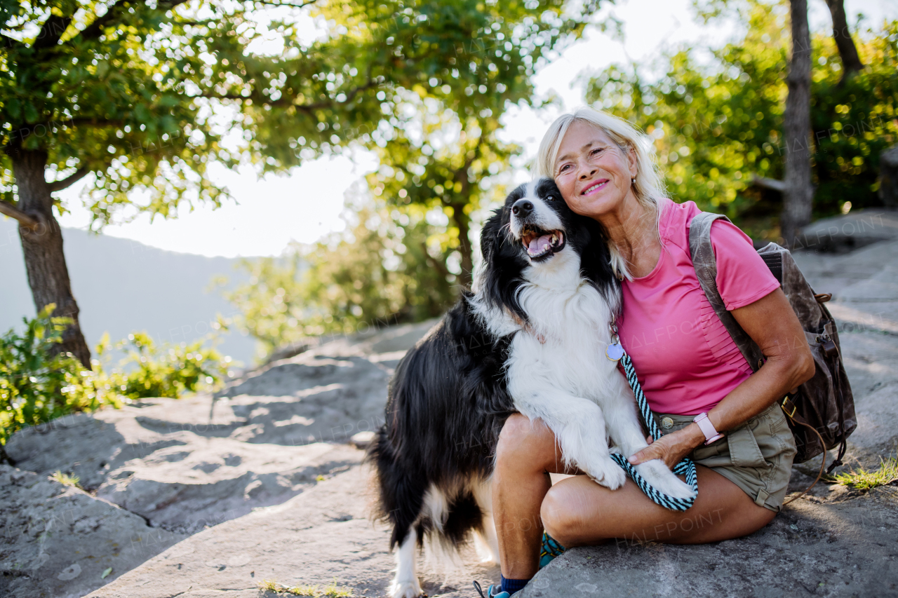 Senior woman resting and stroking her dog during walking in a forest.
