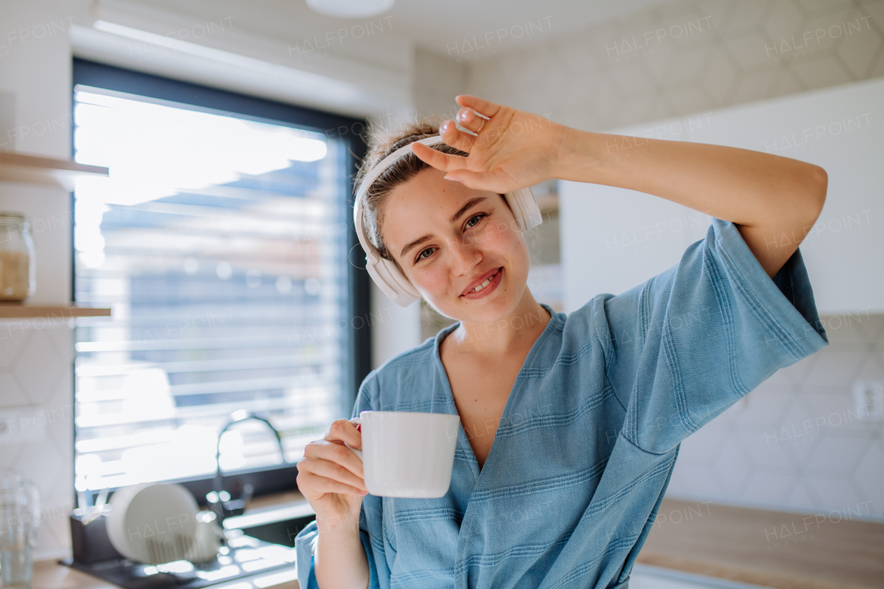 Young woman enjoying cup of coffee and listening music at morning, in a kitchen.
