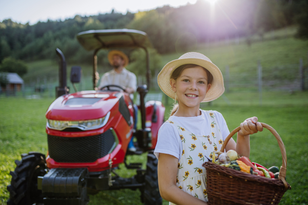Portrait of girl on farm holding harvest basket full of fresh vegetables. Harvesting crops, collecting vegetables on family farm. Concept of multigenerational farming.
