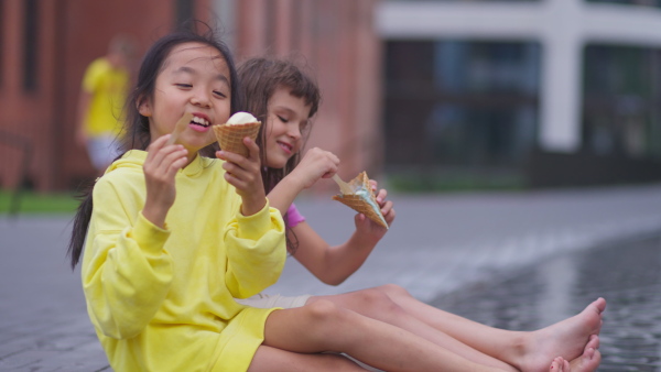 Two girls sitting, having legs in a fountain, enjoying ice cream and summer day.