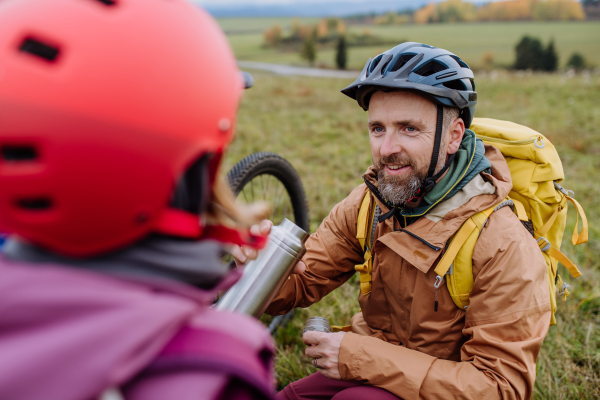 Portrait of father giving cup of warm tea to his daughter. Happy family resting, having snack during hiking together in an autumn mountains.